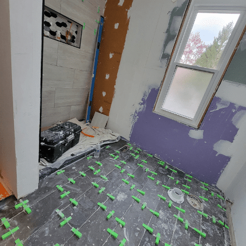 Bathroom wall tile installation using leveling system during renovation by Homes by Covenant`