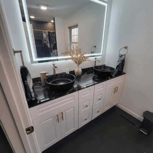 Modern bathroom renovation featuring black countertop double vanity with LED backlit mirror by Homes by Covenant