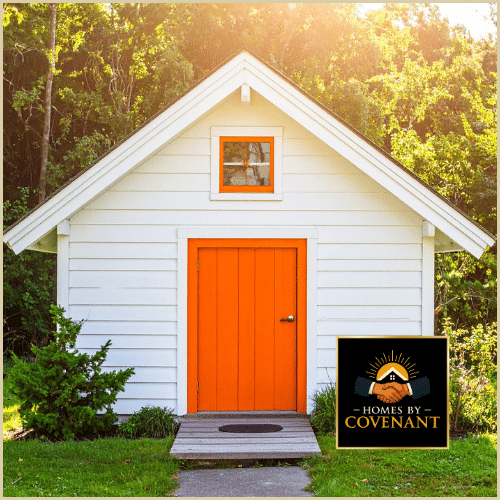 White outdoor shed with bright orange door and front window.