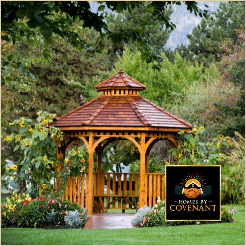 Wooden backyard gazebo with shingled roof and decorative railings.