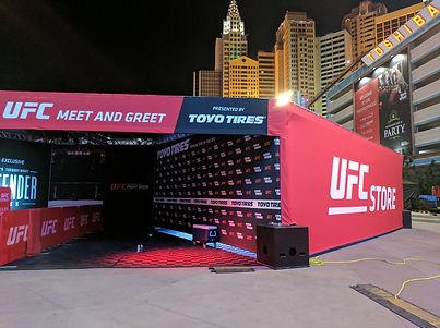 Exterior photo of a UFC fan activation at night with illuminated graphics, entry portal, and crowd area.