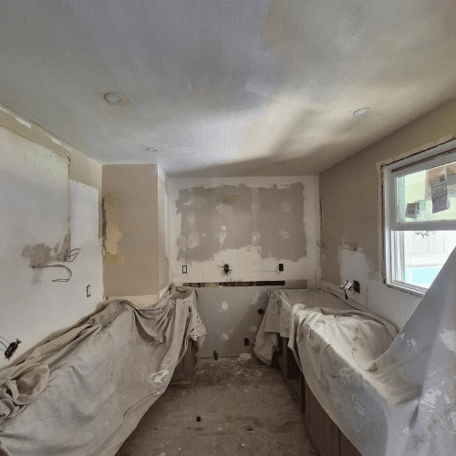 Kitchen renovation by Homes by Covenant during drywall preparation, with cabinets covered and electrical layout ready for backsplash installation.